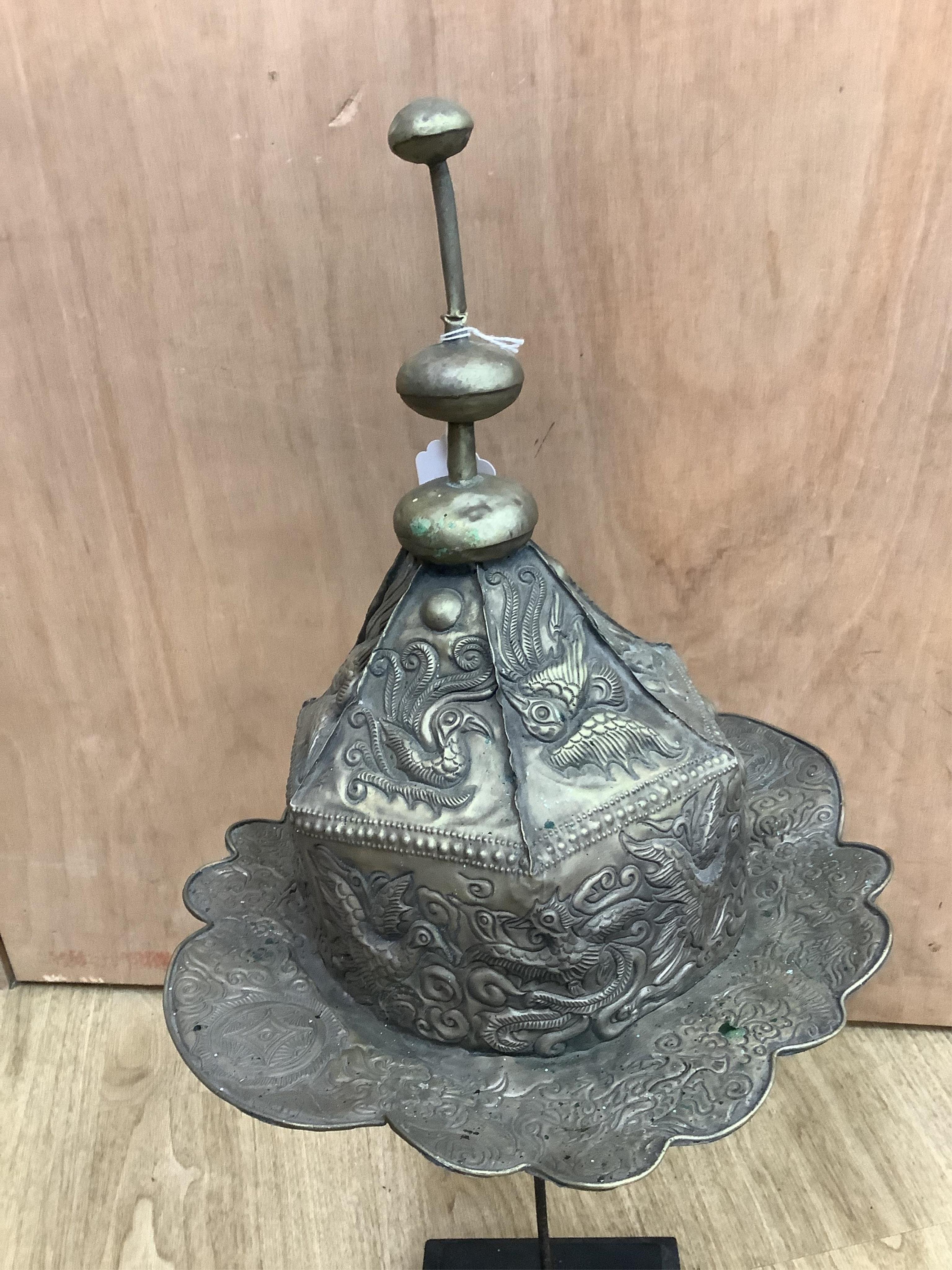 A Chinese Miao tribe embossed metal ceremonial headdress on stand, 63cm high